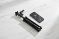 A black smartphone rests next to a collapsed black tripod on a white marble surface.
