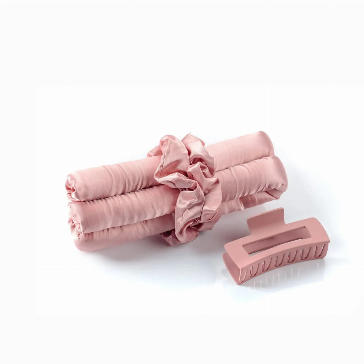 A pink heatless hair curling set features a satin curling rod tied with a matching scrunchie alongside a coordinating claw clip.