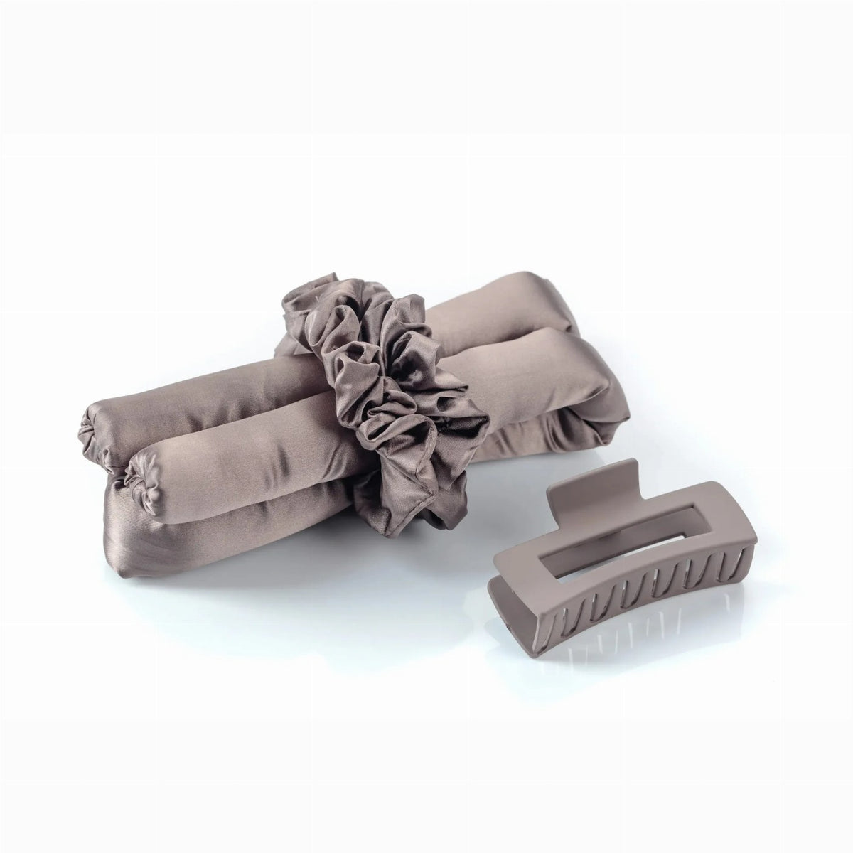 A taupe heatless curling rod with matching silk scrunchies and a claw clip rests on a white background.
