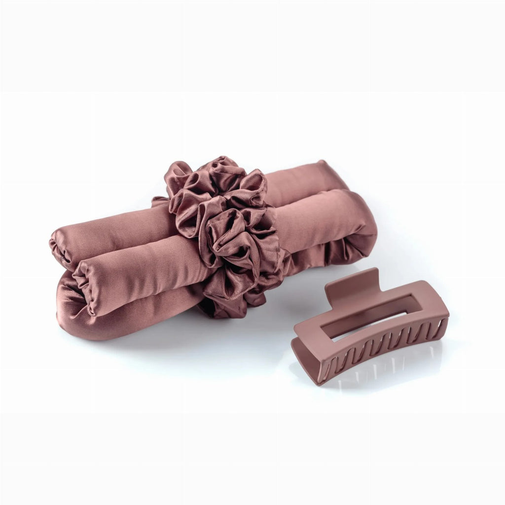 A mauve satin heatless hair curler rod lies next to a matching matte claw clip against a white background.