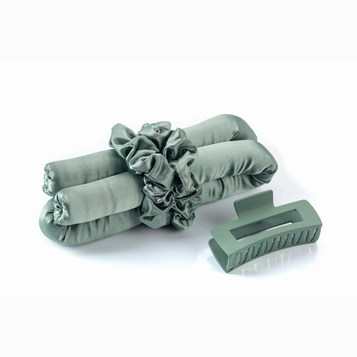 A sage green satin heatless hair curler set rests neatly on a white surface alongside a matching hair claw clip and two scrunchies.