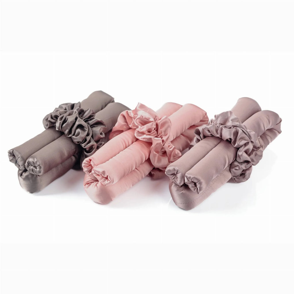 Three silk heatless hair curlers in taupe, pink, and mauve are neatly displayed with matching scrunchies against a white background.